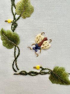 a close up of a piece of embroidery on a white cloth with green leaves and yellow flowers