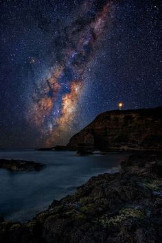 the milky shines brightly in the night sky over the ocean and rocky shore line