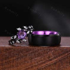 a purple diamond ring sitting on top of a wooden table next to a black wedding band