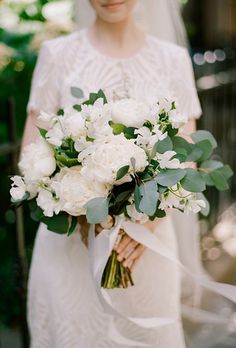 a bride holding a bouquet of white flowers and greenery on her wedding day in instagram