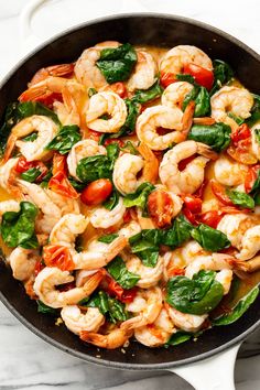 shrimp with spinach and tomatoes in a skillet on a marble countertop, ready to be cooked