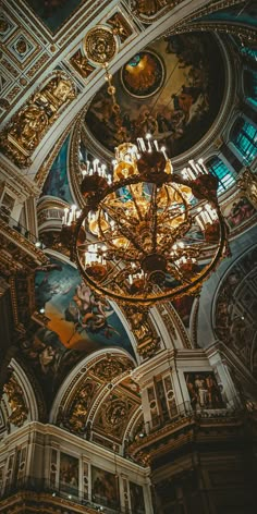 an ornate chandelier hangs from the ceiling in a large room with paintings on it