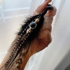 a person holding a feather with beads and pearls on it's end, in front of a window