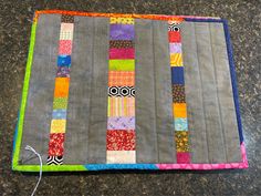 a quilted table runner with colorful strips on the edge and an electric cord hooked up to it