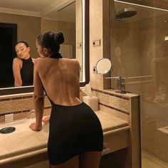 a woman standing in front of a bathroom mirror looking at herself in the mirror, with her back turned to the camera