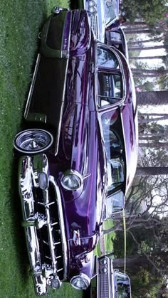 an old purple car is parked in the grass