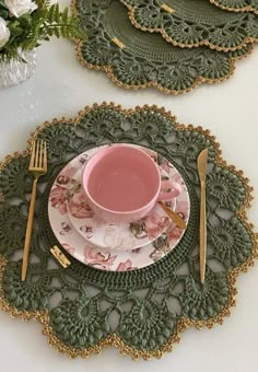 a pink cup and saucer sitting on top of a green doily with gold trim