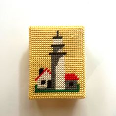 a small needle - beaded square with a lighthouse and dog house on the front