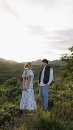 a man and woman standing on top of a lush green hillside