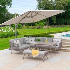 an outdoor patio furniture set with grey cushions and beige umbrella over the table, next to a swimming pool