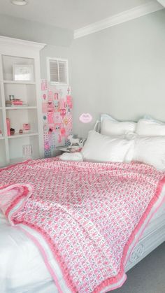 a bed with white sheets and pink bedspread in a room that has shelving on the wall