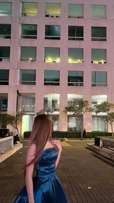 a woman in a blue dress is walking down the street at night with her back to the camera