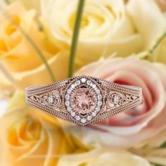 a pink diamond ring sitting on top of some white and yellow flowers with roses in the background