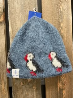 a knitted hat with two penguins on it hanging from a wooden fence, next to a tag