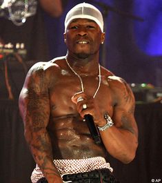 a shirtless man holding a microphone in his right hand and wearing a white hat