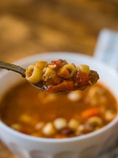 a spoon full of soup on top of a white bowl filled with beans and meat