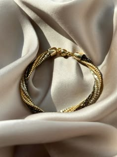 a gold and black bracelet sitting on top of a white satin material covered table cloth