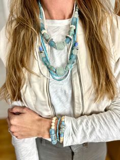 a woman with long hair wearing a white jacket and blue beads on her necklaces