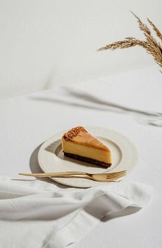 a piece of cheesecake on a white plate with a fork and some dry grass in the background