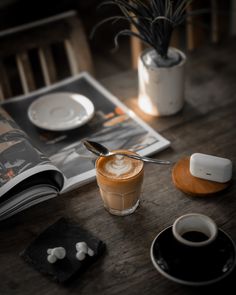 an open magazine sitting on top of a wooden table next to a cup of coffee