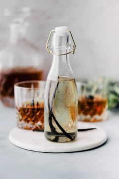 a bottle filled with liquid sitting on top of a white plate next to two glasses