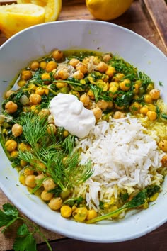 a white bowl filled with vegetables and rice on top of a wooden table next to lemons