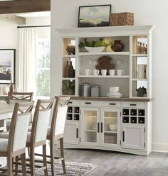 a dining room table and chairs in front of a white hutch with glass doors