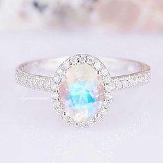 a ring with an oval shaped rainbow colored stone surrounded by diamonds