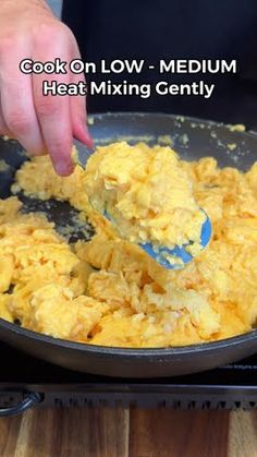 a person scooping scrambled eggs into a skillet