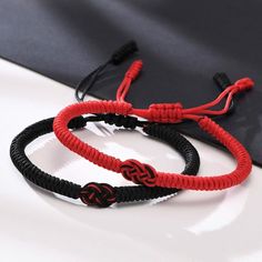 two red and black rope bracelets on top of a white table next to a black bag