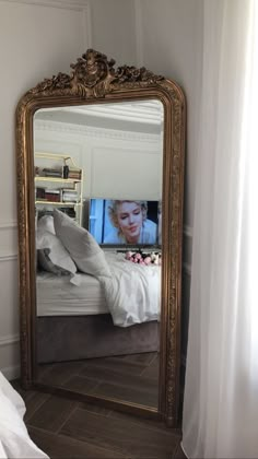 a large gold framed mirror sitting on top of a wooden floor next to a bed