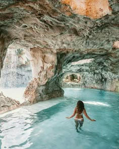 a woman standing in the middle of a pool surrounded by rock formations and blue water