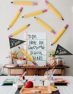 there are many pencils hanging on the wall in front of this table that is decorated with school supplies