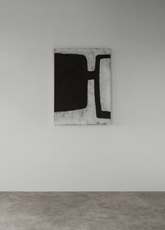 a black and white painting hanging on the wall in an empty room with concrete flooring