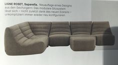 a large sectional sofa with ottomans in front of a white wall that has an advertisement on it