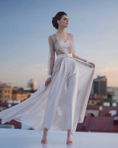 a woman standing on top of a roof wearing a white dress