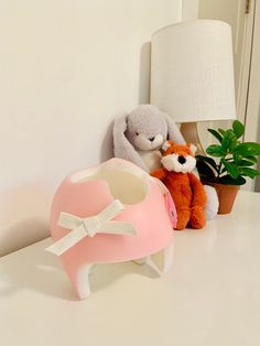 two stuffed animals sitting next to each other on a white table with a lamp and potted plant