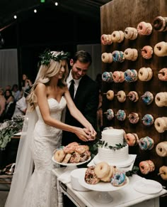 a bride and groom cutting their wedding cake at the reception table with doughnuts on the wall behind them