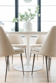 a white table with four chairs around it and a vase filled with flowers on top