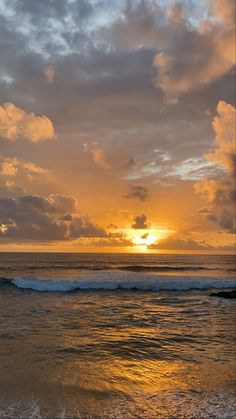 the sun is setting over the ocean with clouds in the sky and waves crashing on the beach