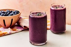 two glasses filled with blueberry smoothie next to a bowl full of blueberries