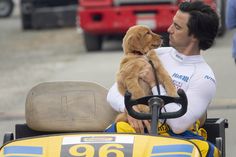 a man holding a puppy in his lap while sitting on a cart with other people behind him