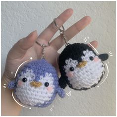 two small crocheted keychains in the shape of penguins are being held by someone's hand