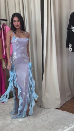 a woman standing in front of a dress hanging on a rack next to a curtain