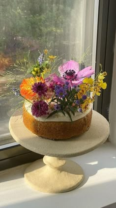 a cake sitting on top of a window sill with flowers in the bottom tier