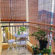 the balcony is decorated with plants and potted plants on the table, along with two white folding chairs