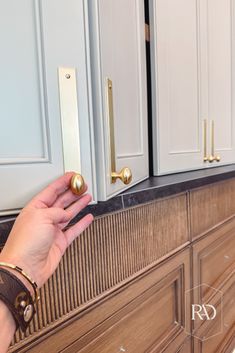 a person is holding the door knobs on a kitchen cabinet that has been painted white and gold