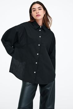 Our Ezra Shirt is a capsule wardrobe dream for your closet. Crafted from 100% crisp European poplin cotton, she offers a classic button-up silhouette in front, but with a cropped back for modern edge. Say hello, as well, to her diagonal seams at the front, sleek collar and long dolman sleeves finished with mother-of-pearl button cuffs. Wear Ezra tucked, tied or open and free—she never fails to inspire new looks.[SPLIT] Rocio, in black and in light blue, is 5'9.5" (175 cm) tall, wearing size XS. Chic Poplin Shirt For Work, Chic Poplin Tops For Workwear, Chic Daywear Poplin Top, Chic Poplin Top For Daywear, Chic Collared Poplin Top, Chic Poplin Top With Relaxed Fit, Daywear Poplin Tops With Button Closure, Daywear Tops With Button Closure, Poplin Tops With Button Closure For Work