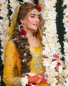 a woman wearing a yellow outfit with flowers in her hair and holding a flower garland