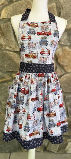 a mannequin wearing a dress with cars and trucks printed on the front, in front of a stone wall